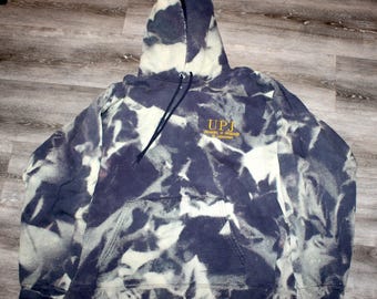 May include: A navy blue hoodie with a white tie-dye pattern. The hoodie has a drawstring hood, a front pocket, and the text "UPJ University of Pittsburgh at Johnstown" in gold lettering.