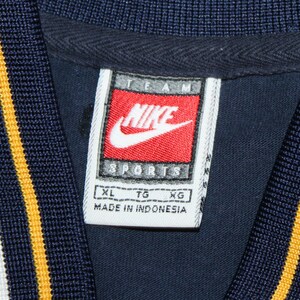 Pu&ograve; includere: Etichetta bianca con testo nero che recita "TEAM NIKE SPORTS" con un logo Nike swoosh rosso. L'etichetta ha anche testo nero che recita "XL TG XG MADE IN INDONESIA".