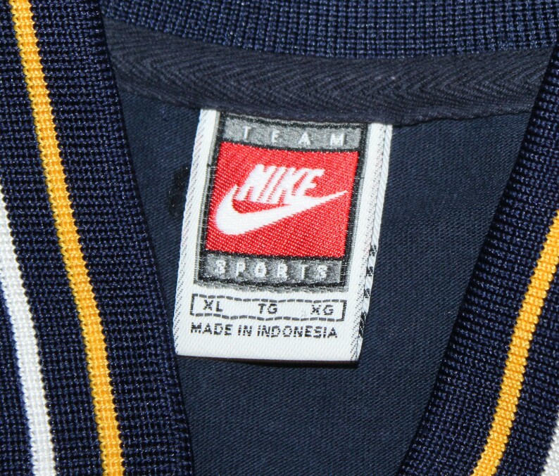 Pu&ograve; includere: Etichetta bianca con testo nero che recita "TEAM NIKE SPORTS" con un logo Nike swoosh rosso. L'etichetta ha anche testo nero che recita "XL TG XG MADE IN INDONESIA".