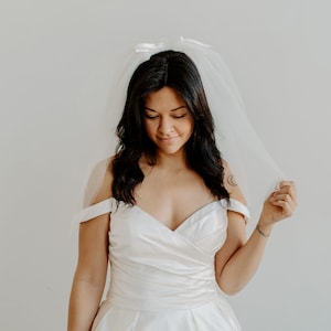 Op de afbeelding: Een bruid in een witte, off-shoulder bruidsjurk met een tule sluier.