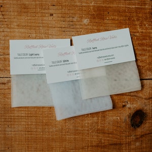 Pu&ograve; includere: Tre campioni di tessuto tulle su una superficie di legno. I campioni sono etichettati "Light Ivory", "White" e "Ivory". Ogni campione &egrave; abbinato a una scheda di "Ruffled Rose Vets" con il nome del colore del tulle.