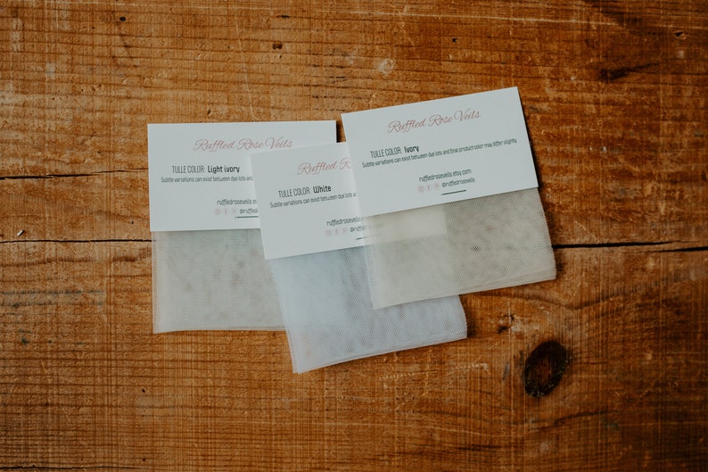 Pu&ograve; includere: Tre campioni di tessuto tulle su una superficie di legno. I campioni sono etichettati "Light Ivory", "White" e "Ivory". Ogni campione &egrave; abbinato a una scheda di "Ruffled Rose Vets" con il nome del colore del tulle.