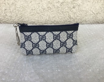 May include: A small, blue and white patterned zippered pouch with a silver key chain attached. The pouch has a black trim and a repeating pattern of the Gucci logo.