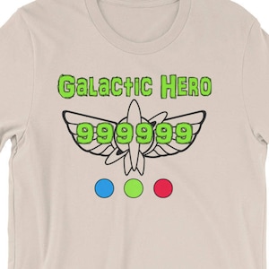 May include: A beige t-shirt with a green graphic of a spaceship with the text "Galactic Hero 999999" printed on the front.
