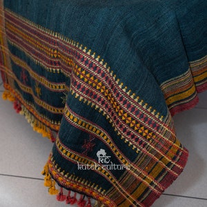May include: A dark teal blue woven throw blanket with a colorful geometric pattern border. The blanket has a fringe edge and is made of wool.