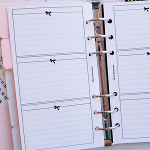 May include: A white planner with black lines and a black bow on each page. The planner has a silver binder with rings. The text "Peach Blossoms" is written on the side of the planner. The text "TODAY" is written on a pink sticky note.