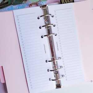 May include: A white planner with a pink cover and silver rings. The planner has a lined page with the text "Peach Blossoms" on the left and right pages. The planner has a small heart design on the right page.