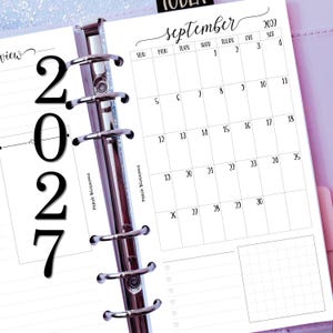 May include: A ring-bound planner insert featuring a September 2027 calendar page. The white paper has black text, including the month name, days of the week, and dates. A vertical silver metal binder mechanism with six rings runs down the centre.
