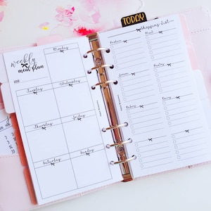 May include: A pink and white planner with a weekly meal plan section and a shopping list section. The shopping list section is divided into categories: produce, meat, frozen, pantry, bakery, and dairy.