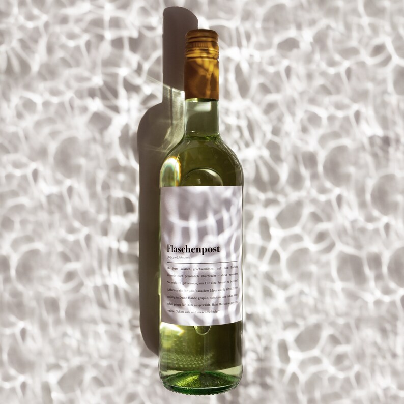 May include: A clear glass bottle of white wine with a white label that says "Flaschenpost" in black text. The bottle is sitting on a white surface with a pattern of light and dark areas.
