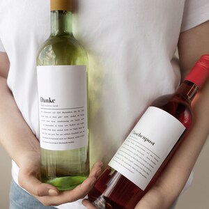May include: Two glass bottles of wine with white labels. The bottle on the left has a white label with the word "Danke" and a German message. The bottle on the right has a white label with the word "Flaschenpost".