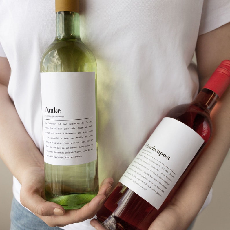 May include: Two glass bottles of wine with white labels. The bottle on the left has a white label with the word "Danke" and a German message. The bottle on the right has a white label with the word "Flaschenpost".