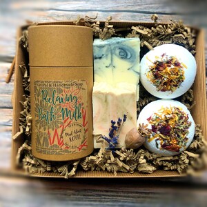 May include: A gift box filled with bath products. The box contains two bath bombs with dried flowers, a bar of soap, and a tube of bath milk. The bath milk tube has a label that reads "Natural & Handmade Soap Relaxing Bath Milk Mad About Nature madaboutnature.uk".