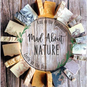 May include: A variety of handmade soap bars arranged in a circle on a wooden background. The soaps are in various colors and patterns, including brown, white, gray, and green. The text "Kind on the Environment" and "Mad About Nature" is written in a circle around the soaps. The text "Gentle on the Skin" is written below the soaps.