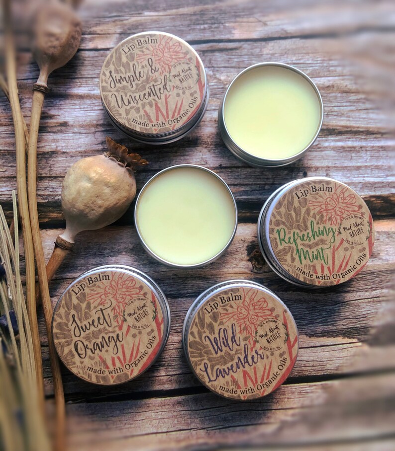 May include: Five small round metal tins of lip balm with brown paper labels. The labels have illustrations of flowers and the text "Lip Balm" and different flavors: "Simple & Unscented", "Sweet Orange", "Wild Lavender", "Refreshing Mint".