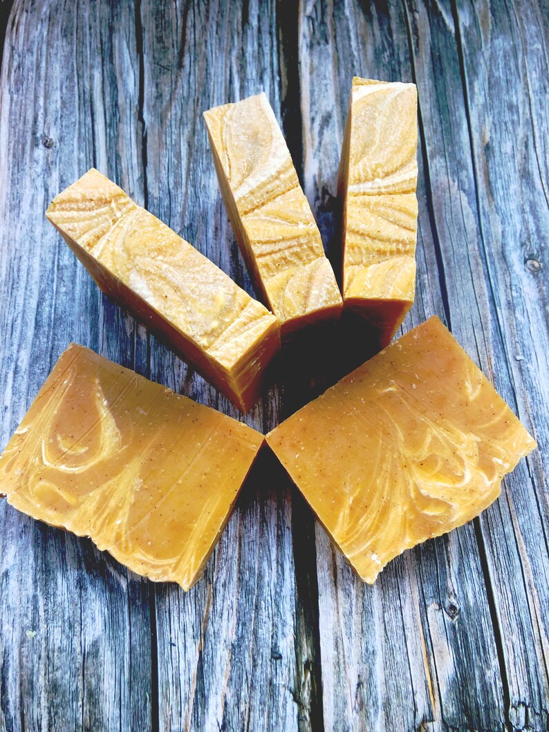 May include: Five bars of handmade soap with a swirl pattern in shades of yellow and white. The soap is arranged in a star shape on a wooden surface.