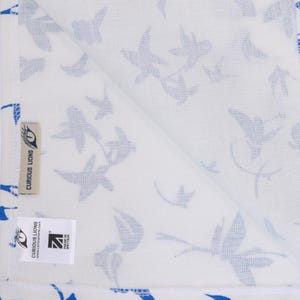 May include: A white textile featuring a repeating pattern of blue bird silhouettes. The fabric includes a beige tag with the text CURIOUS LIONS and a white rectangular label displaying the text CURIOUS LIONS, curiouslions.com, and MADE IN BRITAIN.