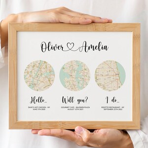 May include: A framed print featuring three circular map illustrations. The text "Oliver & Amelia" is above the maps. Below the maps are the phrases "Hello...", "Will you?", and "I do..." with dates and locations.