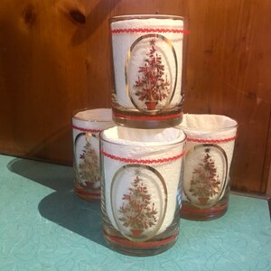 May include: Set of four clear glass tumblers with a gold rim and a red and gold Christmas tree design. Each tumbler has a white paper coaster with a red trim.