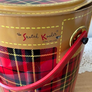 Peut inclure: Une glaci&egrave;re en m&eacute;tal rouge, noir et jaune &agrave; carreaux avec une poign&eacute;e rouge et le texte "the Skotch Kooler 4 GAL. DE LUXE" sur le c&ocirc;t&eacute;.