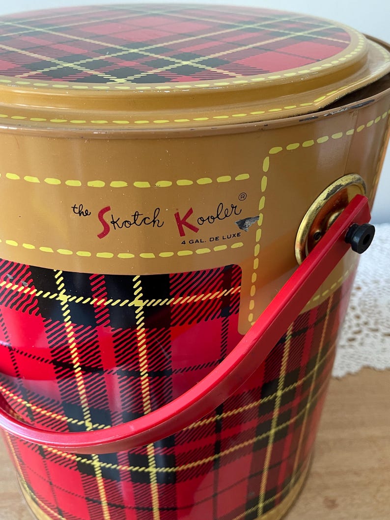 Peut inclure: Une glaci&egrave;re en m&eacute;tal rouge, noir et jaune &agrave; carreaux avec une poign&eacute;e rouge et le texte "the Skotch Kooler 4 GAL. DE LUXE" sur le c&ocirc;t&eacute;.