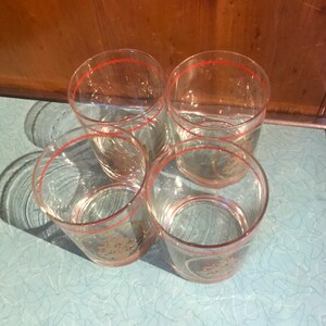 May include: Set of four clear glass tumblers with a red rim and gold accents. The glasses have a textured design.