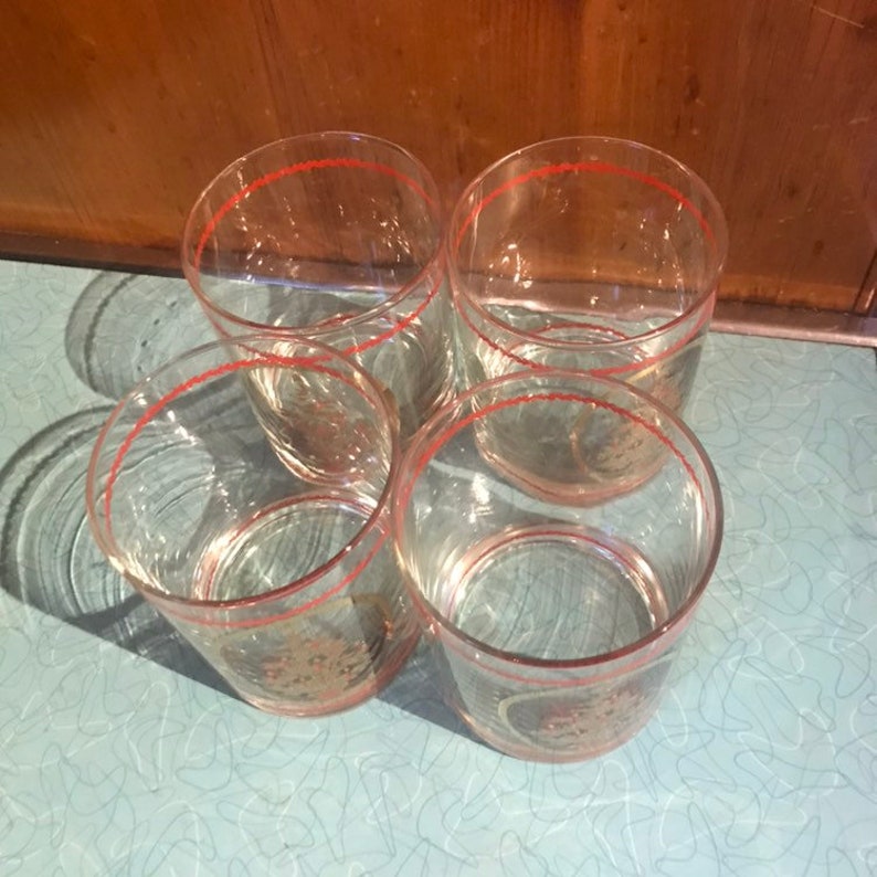 May include: Set of four clear glass tumblers with a red rim and gold accents. The glasses have a textured design.