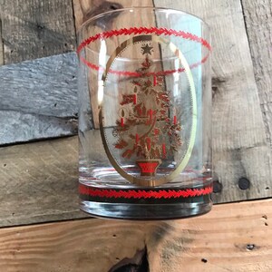 May include: A clear glass tumbler with a gold and red Christmas tree design. The tree is decorated with gold stars and red candles.