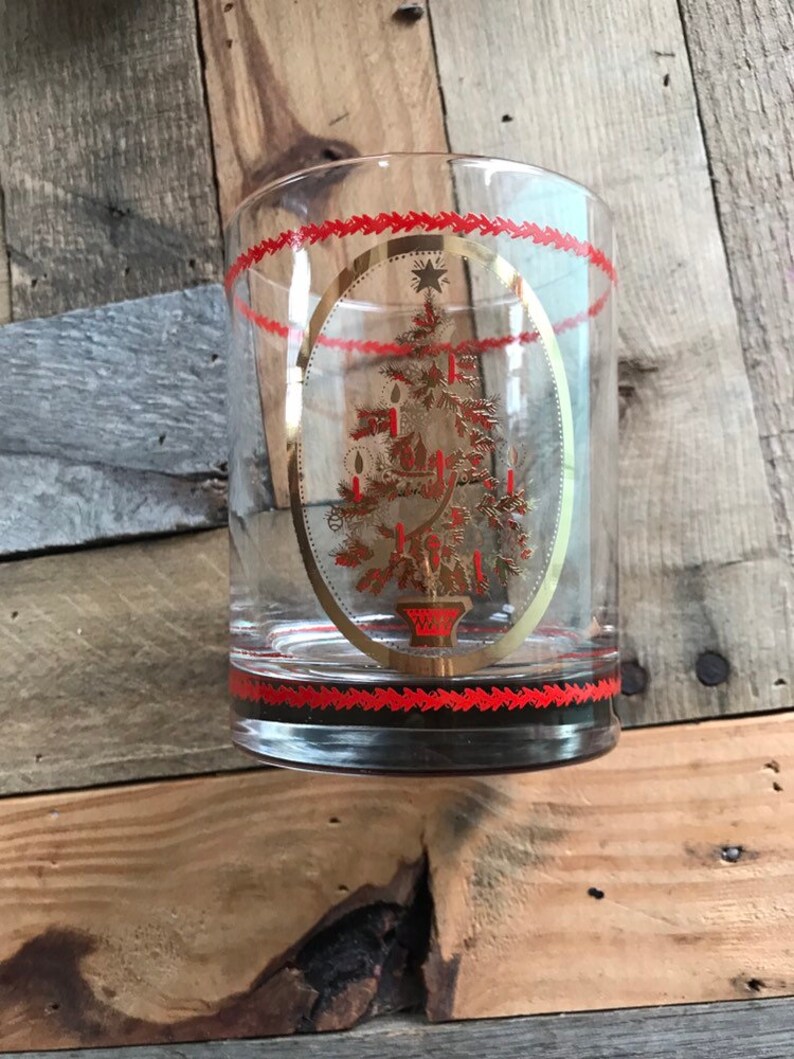 May include: A clear glass tumbler with a gold and red Christmas tree design. The tree is decorated with gold stars and red candles.