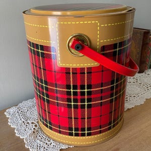 Peut inclure: Une glaci&egrave;re en m&eacute;tal rouge, noir et jaune &agrave; carreaux avec une garniture en simili cuir marron et une poign&eacute;e rouge.