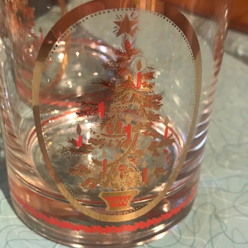 May include: A clear glass tumbler with a gold and red rim. The tumbler features a gold Christmas tree design with red candles.