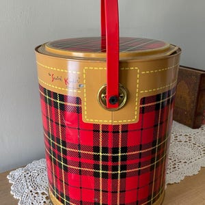 Peut inclure: Glaci&egrave;re rouge et noire &agrave; carreaux avec un dessus brun et une poign&eacute;e rouge. La glaci&egrave;re porte l'inscription "The Scotch Kooler" sur le c&ocirc;t&eacute;.