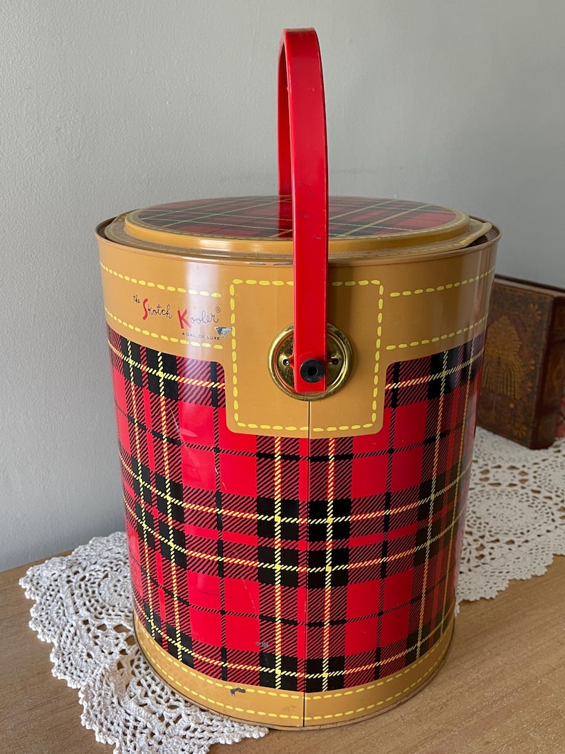 Peut inclure: Glaci&egrave;re rouge et noire &agrave; carreaux avec un dessus brun et une poign&eacute;e rouge. La glaci&egrave;re porte l'inscription "The Scotch Kooler" sur le c&ocirc;t&eacute;.