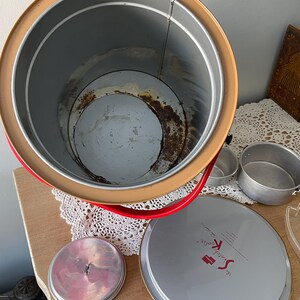 Peut inclure: Une glaci&egrave;re vintage en m&eacute;tal rouge et jaune avec un couvercle blanc. Le couvercle porte l'inscription "The Scotch Boy". La glaci&egrave;re est ouverte et vide.