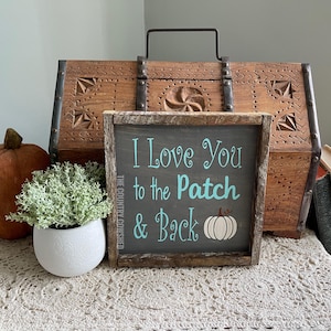 May include: A rustic wooden sign with the text "I Love You to the Patch & Back" in teal blue lettering. A white pumpkin silhouette is next to the text "Back".