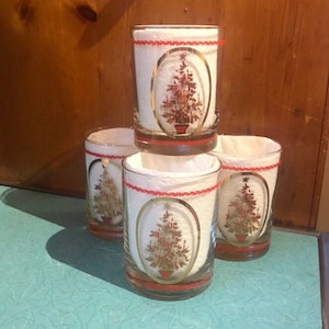 May include: Set of four clear glass tumblers with a red and gold trim. Each tumbler features a Christmas tree design with red and green accents.
