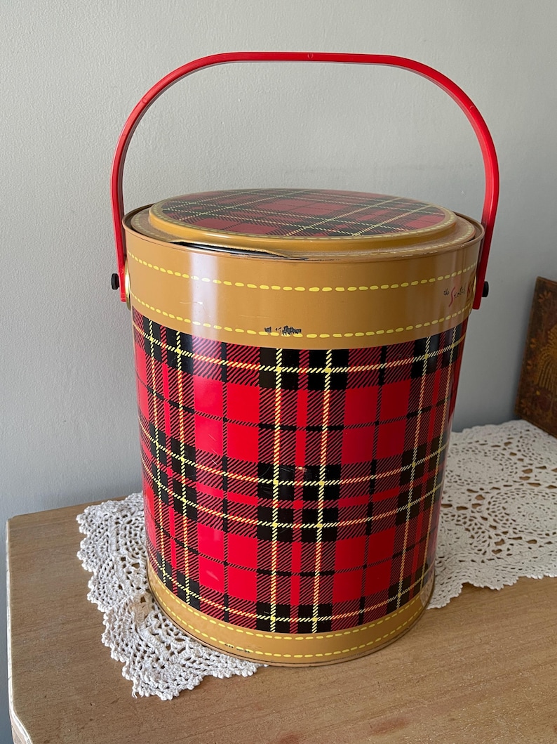 Peut inclure: Une glaci&egrave;re en m&eacute;tal rouge et noir &agrave; carreaux avec une poign&eacute;e rouge. La glaci&egrave;re est orn&eacute;e d'une bordure jaune autour du haut et du bas.