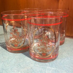 May include: Set of four clear glass tumblers with a gold and red design. Each tumbler features a stylized Christmas tree with gold ornaments and candles.