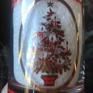 May include: A clear glass tumbler with a gold and red Christmas tree design. The tree is decorated with red candles and gold ornaments. The glass has a red and white border.