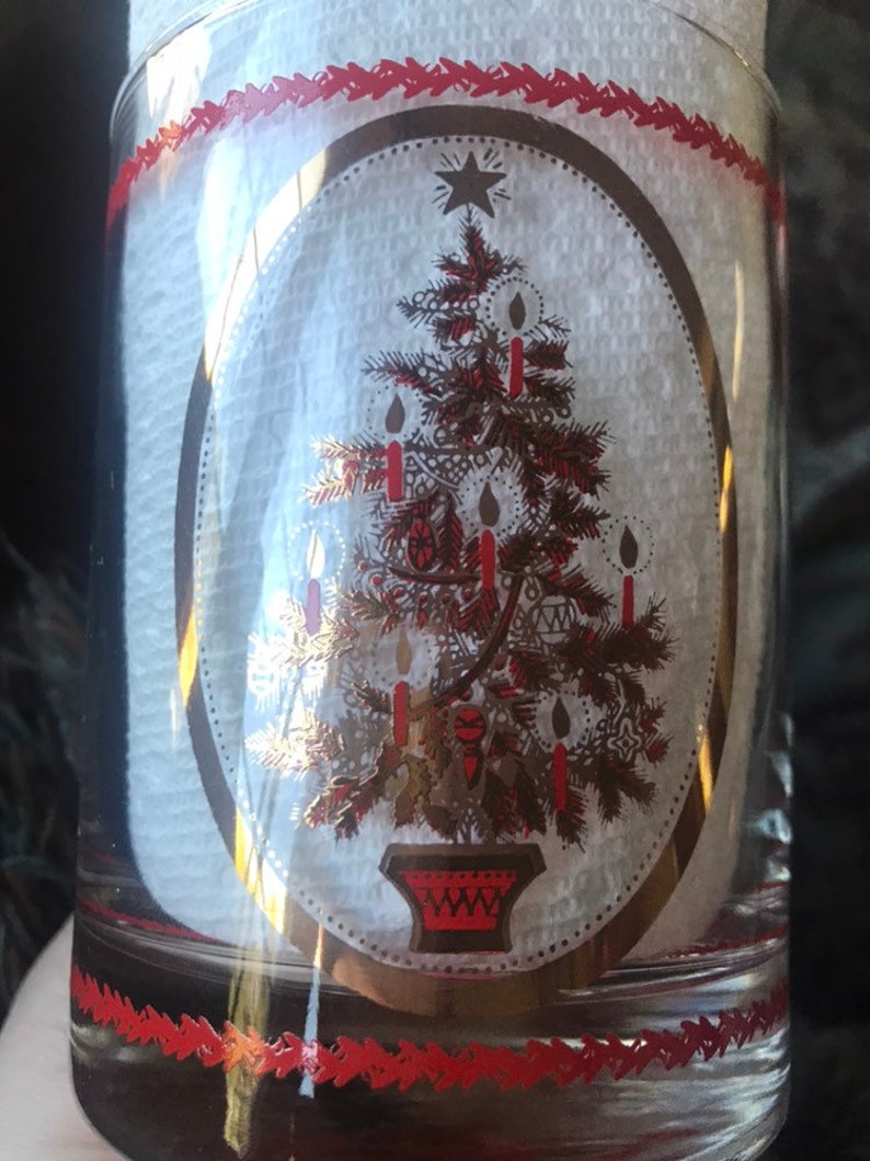 May include: A clear glass tumbler with a gold and red Christmas tree design. The tree is decorated with red candles and gold ornaments. The glass has a red and white border.