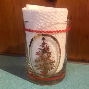 May include: A clear glass tumbler with a red and gold Christmas tree design. The tree is decorated with gold ornaments and red candles. The tumbler has a red band around the top and bottom.