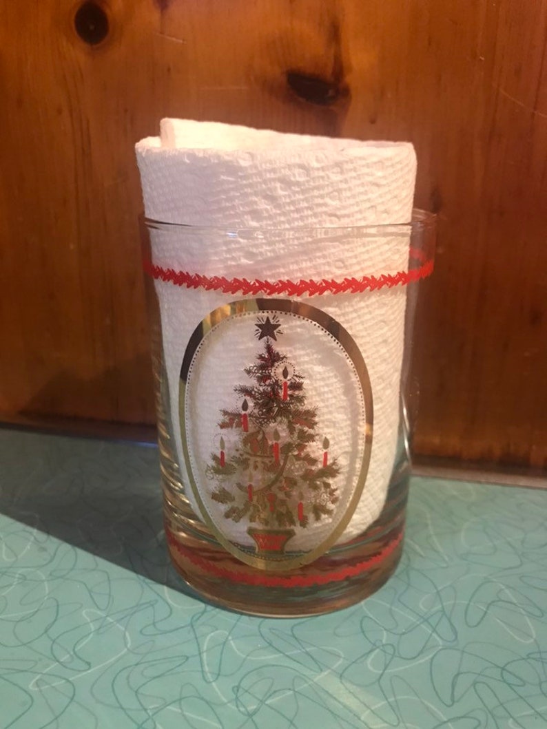 May include: A clear glass tumbler with a red and gold Christmas tree design. The tree is decorated with gold ornaments and red candles. The tumbler has a red band around the top and bottom.