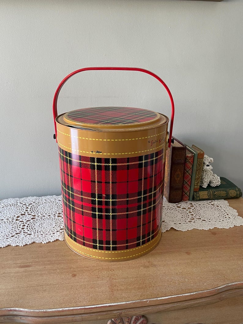 Peut inclure: Glaci&egrave;re en m&eacute;tal rouge et noir &agrave; carreaux avec une poign&eacute;e rouge. La glaci&egrave;re a une bordure jaune et le texte "The Scotch Kilt" est visible sur le c&ocirc;t&eacute;.