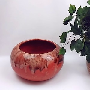 May include: A large, round, orange ceramic planter with brown and white glaze. The planter has a wide opening and a rounded bottom.