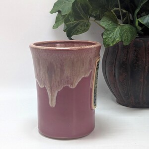 May include: A cylindrical ceramic mug featuring a solid mauve base and a lighter, cream-colored glaze that drips down from the rim. The mug has a smooth, glossy finish and a straight-sided profile, showcasing a distinct two-tone color transition.