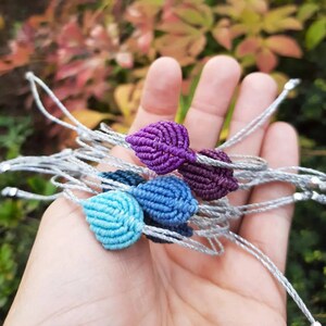 Può includere: Un set di braccialetti dell'amicizia fatti a mano con ciondoli a forma di foglia in tonalità di viola, blu e turchese. I braccialetti sono realizzati con un cordoncino argentato e hanno un design semplice ed elegante.