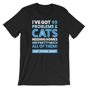 Puede incluir: Camiseta negra con un gr&aacute;fico azul y blanco que dice "Tengo 99 problemas & gatos que necesitan hogar, son casi todos! Amar, acoger, adoptar"