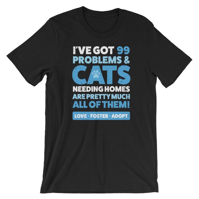 Puede incluir: Camiseta negra con un gr&aacute;fico azul y blanco que dice "Tengo 99 problemas & gatos que necesitan hogar, son casi todos! Amar, acoger, adoptar"