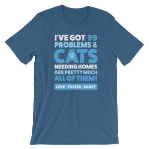 Puede incluir: Una camiseta azul con un gr&aacute;fico blanco que dice "Tengo 99 problemas y gatos que necesitan hogar, casi todos! Amor, acogida, adopci&oacute;n."