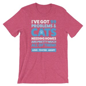 Puede incluir: Una camiseta rosa jaspeada con un gr&aacute;fico azul que dice "Tengo 99 problemas & gatos que necesitan hogar, casi todos! Amar, acoger, adoptar."